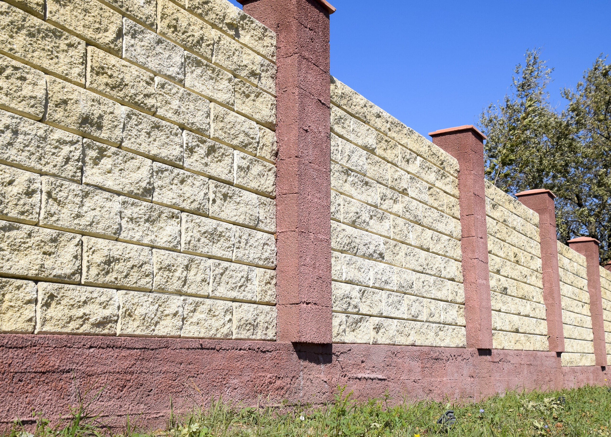 Fence made of bricks and decorative plaster. Yellow fence with red elements. High and beautiful fencing